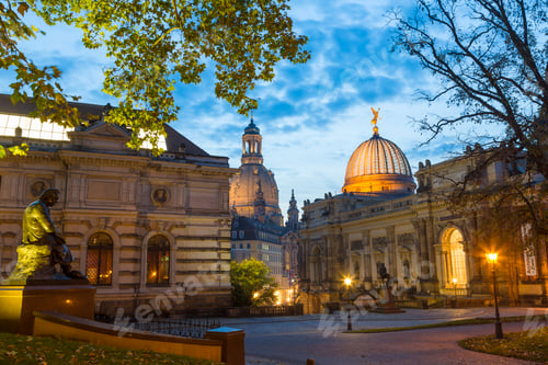 Preview: Illuminated town square with facades of domed church, college and sculptures.