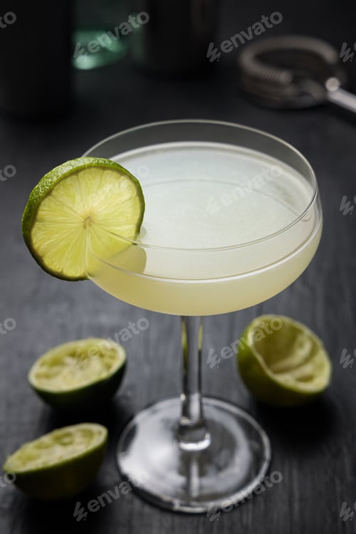 Preview: Classic Daiquiri Cocktail with a lime wheel. Squeezed limes over a black table