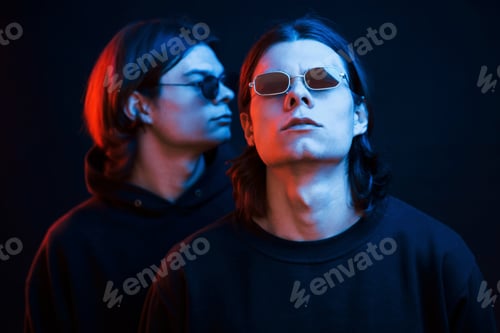 Preview: Standing in the black clothes. Portrait of twin brothers. Studio shot in dark studio with neon light