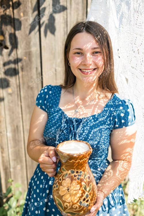 Preview: Young farmer woman smiling on camera carries jug of milk after milking cow on farm pasture. Natural