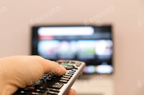Preview: Watching TV and using remote controller. Hand holding TV remote control with a television in the
