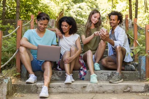 Preview: Multiethnic friends students outdoors using mobile phone and laptop