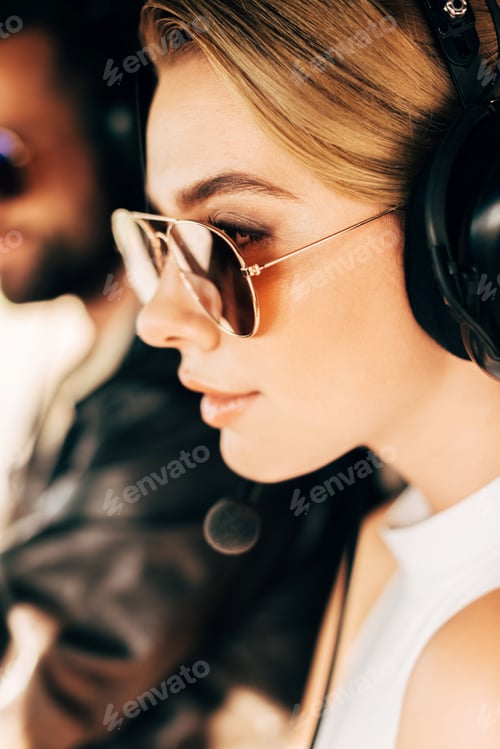 Preview: selective focus of beautiful woman in sunglasses and headset sitting near male pilot in cabin of