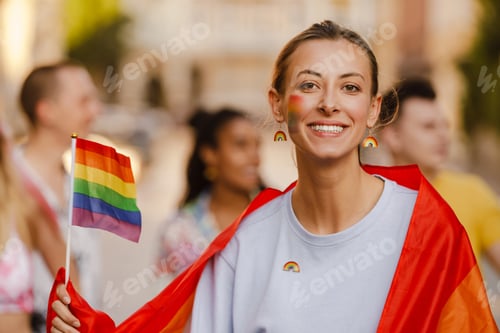 Preview: Young lesbian woman wrapped in rainbow flag smiling during pride parade