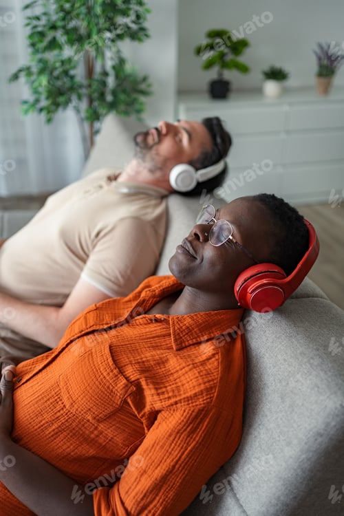 Preview: Serene couple relaxing on sofa, enjoying music with headphones