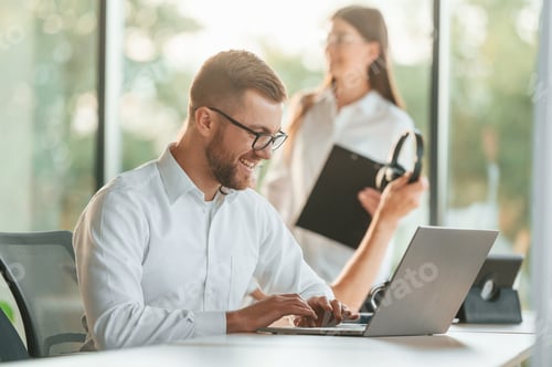Preview: Working by using laptop. Man and woman are in the modern office together