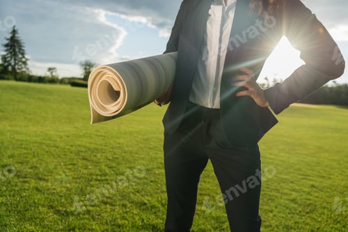 Preview: partial view f businesswoman standing akimbo with yoga mat in hand in park