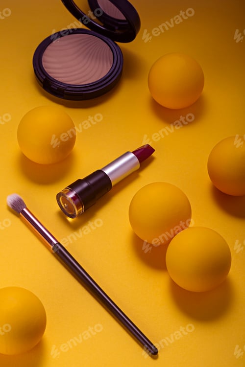 Preview: Makeup lipstick and cosmetics on yellow background seen from above.