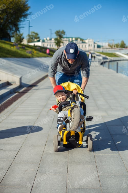 Preview: dad walks with his son along the embankment. carries him on a bicycle stroller