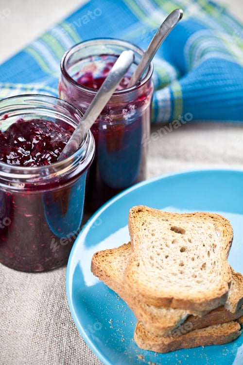 Preview: Toasted cereal bread slices on blue ceramic plate and homemade cherry and wild berries jam in jars.
