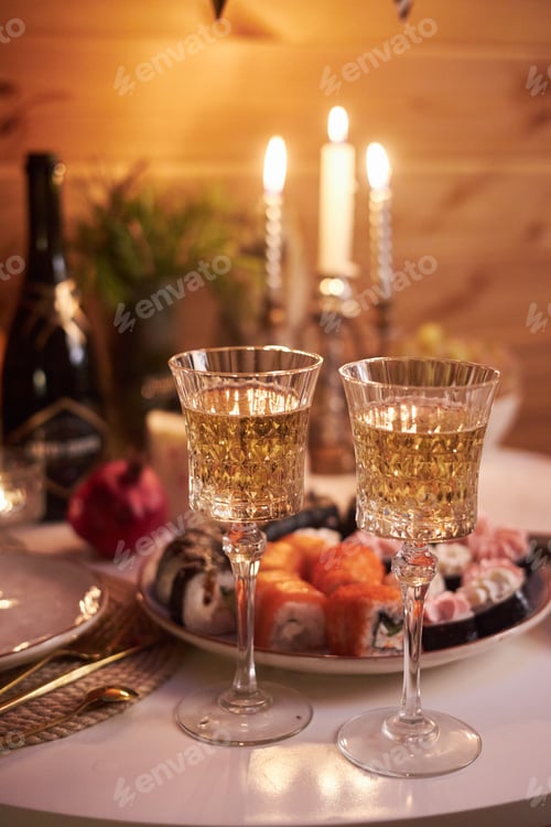 Preview: Two glasses with sparkling drinks sit on a table next to a plate of sushi. Candles are lit