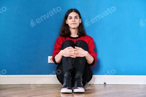 Preview: Portrait of young teenage guy sitting on the floor on blue background