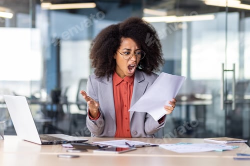 Preview: Furious female head of company reading important document with bad news while sitting by office