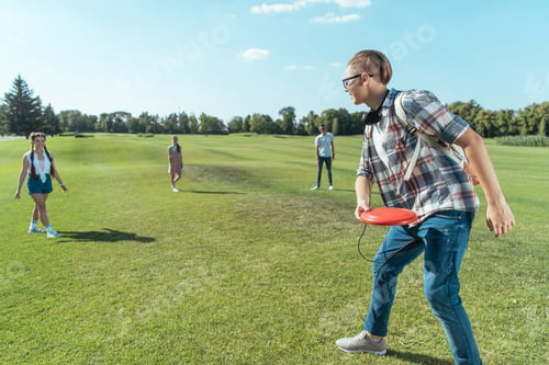 Preview: group of happy teenage friends playing with flying disc in park