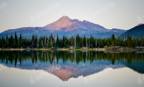 Preview: Scenic view of a lake reflecting green forests and mountains on its shore at sunset
