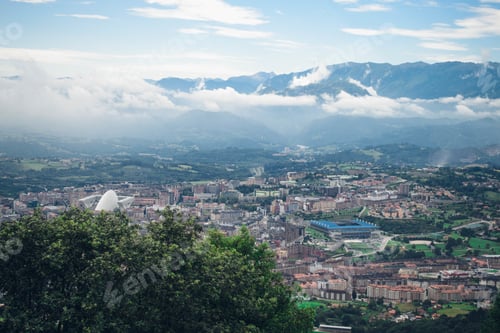 Preview: Aerial beautiful shot of the city under a blue cloudy sky with trees on the foreground