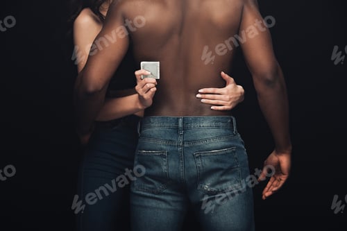 Preview: partial view of woman embracing shirtless african american man and holding condom isolated on black