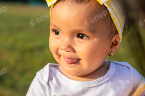 Preview: beautiful brown-skinned latina baby girl, showing her tongue on a beautiful summer day