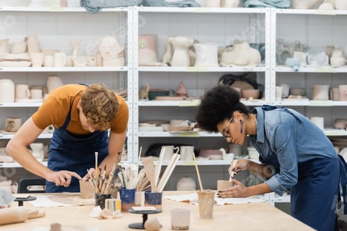 Preview: multiethnic woman and man shaping clay cups during pottery class