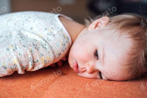 Preview: Little girl lies on the sofa with a sad look