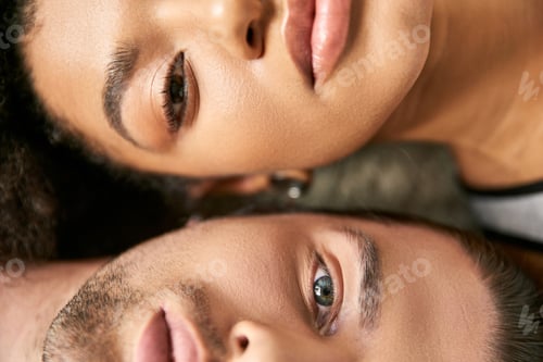 Preview: close up view of attractive sexy multicultural couple lying and looking straight at camera