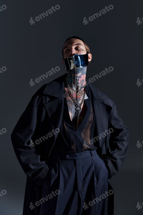 Preview: good looking man with tattoos in laced stylish mask posing on black backdrop, fashion concept