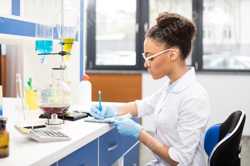 Preview: Side view of young scientist in eyeglasses making experiment and taking notes in research laboratory