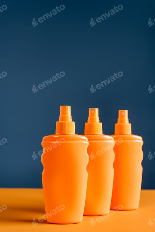 Preview: spray bottles with sunblock on orange surface isolated on blue