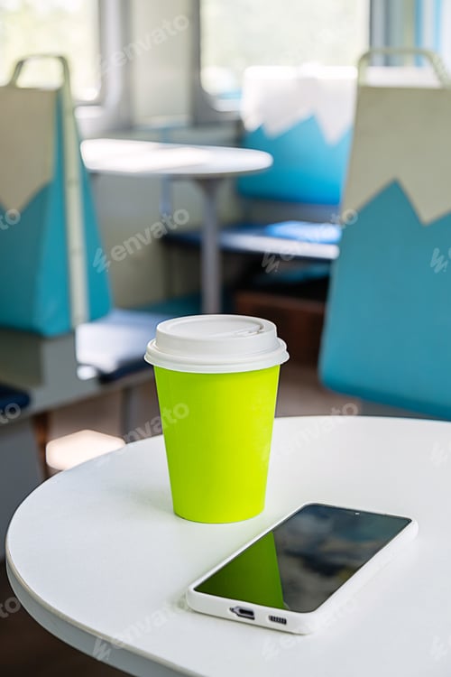 Preview: Focus on a green eco cup and a smartphone on a table inside a train for a solo travel trip.