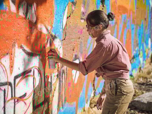 Visualização: Linda jovem fazendo um grafite colorido com spray de aerossol na parede da rua urbana.