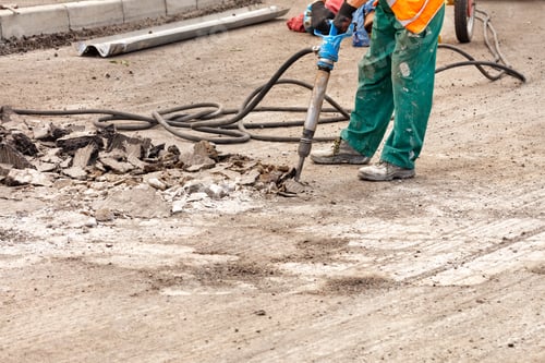 Preview: A road worker breaks up old asphalt with a pneumatic jackhammer on a stretch of road.