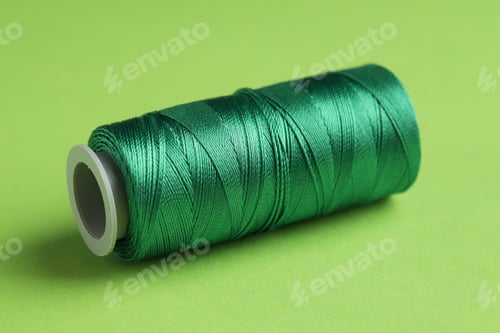Preview: Spool of sewing thread on green background, closeup