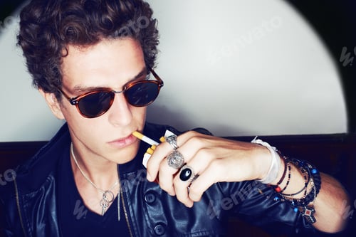 Preview: Closeup shot of a stylish young man pulling a cigarette out of a box with his lips