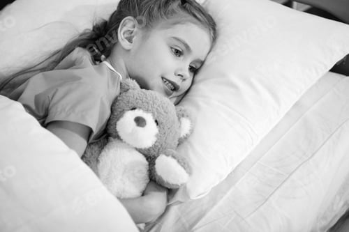 Preview: Smiling little girl with teddy bear lying in hospital bed, black and white photo