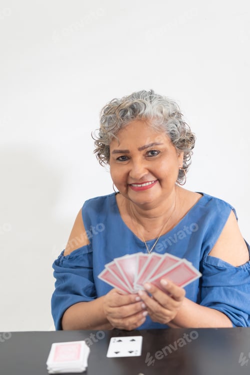 Preview: Happy senior woman playing cards at home, enjoying retirement with a winning hand