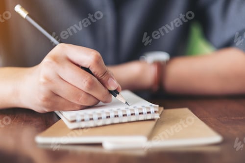Preview: Closeup image of a woman writing on blank notebook on wooden table