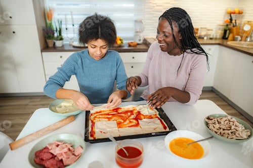 Preview: Mother and daughter making pizza together in home kitchen