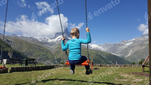 Preview: Child swinging in a park overlooking the mountain matterhorn