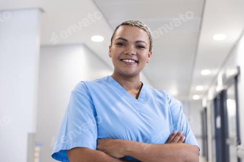 Preview: Portrait of happy biracial female doctor with short hair wearing scrubs in corridor at hospital