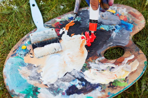Preview: Cropped hand spilling red paint from tube on messy palette