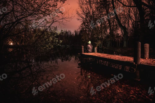 Preview: Man in hood on dock near water between murk forest in redness