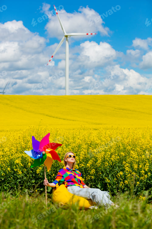 Preview: Beautiful female in 90s stylish shirt with pinwheel sitting in rapeseed field