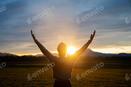 Preview: Woman embracing life standing outside in beautiful meadow with her arms raised high