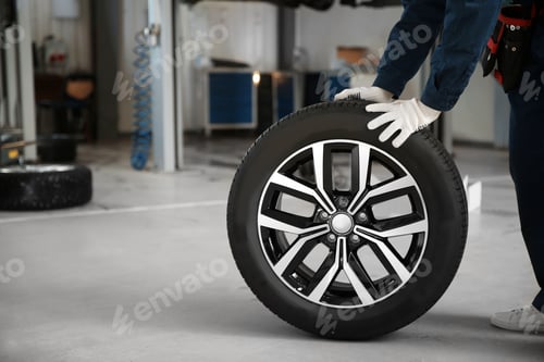 Preview: Technician rolling car wheel in automobile repair shop closeup. Space for text