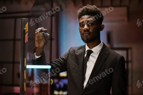 Preview: African-American businessman standing near glass board with sticky notes and writing