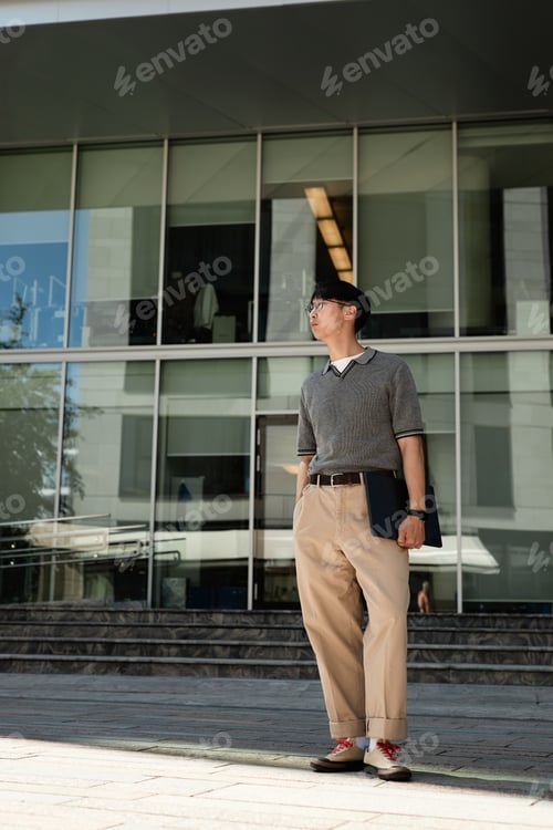 Preview: Male IT Programmer Holding Laptop Standing next to Business Building Outdoors