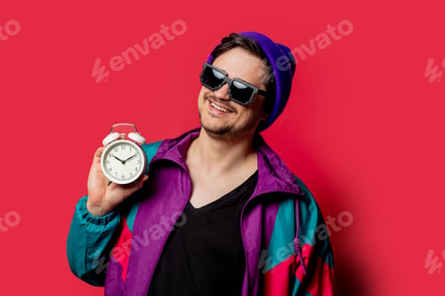 Preview: Funny guy in 80s style jacket and sunglasses holds alarm clock on red backgorund