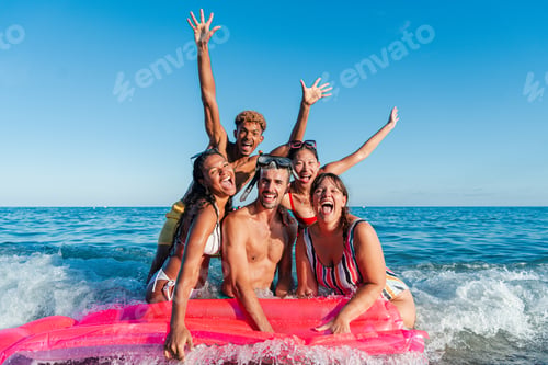 Preview: Group of young friends having fun at the beach, floating on an inflatable mattress by the sea shore
