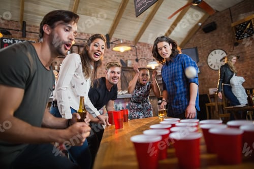 Preview: Young friends enjoying beer pong game in restaurant