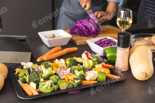 Preview: Midsection of african american woman chopping cabbage, preparing meal using tablet in kitchen